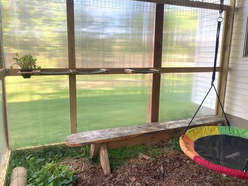 Wooden bench and trampoline in a screened-in outdoor area with green grass outside.