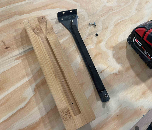 Wooden brackets and a black metal bracket on a wooden surface with a tape measure in the background.