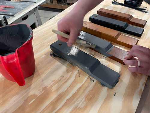 Person using a tool on a wooden surface with various tools in the background