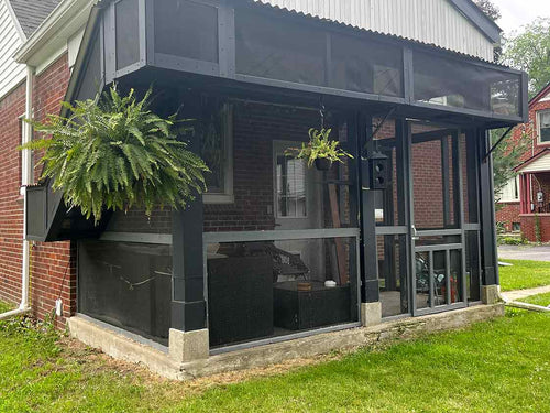 Screened porch attached to a house with plants and furniture