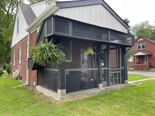 Screened porch attached to a brick house with greenery and neighboring houses in the background.