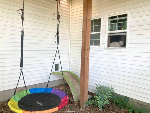 Colorful trampoline swing set attached to a house with a cat looking out a window.